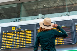 Tourist woman at the airport looking at the information on screens in the connection terminal