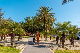 A mother with her son walking through Los Cristianos through a park with palm trees on the island of Tenerife in summer