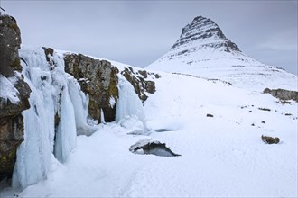 Kirkjufell mountain and the frozen waterfall Kirkjufellsfoss on the Snaefellsnes peninsula in the snow in winter