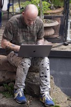 Man with tattooed arms works on laptop in home office in garden