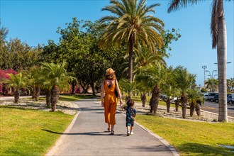 A mother with her son walking through Los Cristianos through a park with palm trees on the island of Tenerife