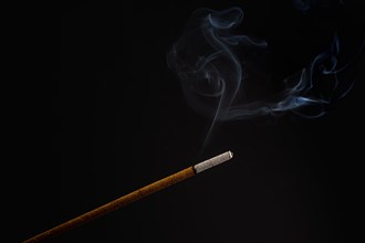 Burning incense stick smoldering on a black background