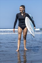 Challenging perceptions: A young woman with a prosthesis surfacing from the sea with her surfboard