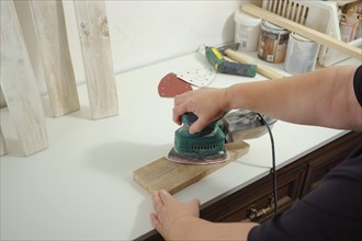 Woman's hands sanding a wooden board with an electric sander in her workshop at home