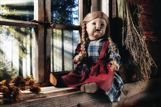 Antique porcelain doll on a rustic window sill with a view of the landscape