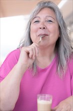 Older white-haired woman sucking on the spoon of her latte on the terrace
