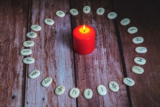Circle of Viking stone runes on a wooden table with a lighted red candle in the center
