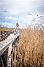 Woman standing on jetty by lake with reeds