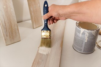 Woman's hands painting white on a wooden board with a paintbrush