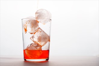 Close-up of a glass with ice pouring strawberry liqueur over the cubes