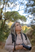 Close-up of a woman photographer with her backpack looking at the trees in the forest