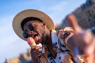 Black ethnic man enjoy summer vacation at the beach eating an ice cream taking a selfie
