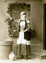 Studio portrait of a woman in traditional Greek dress beside a fountain