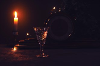 Glass with white wine with vintage old wooden clock and burning yellow candle garland lights on the background. Midnight on clock. Night festive picture for background. Beautiful golden lights