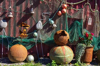 Discarded maritime objects and equipment such as rusty buoys and old fishing nets displayed on the wooden wall of a shed