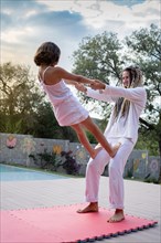 Pretty woman with dreadlocks does acroyoga with her daughter outdoors. Both dressed in white