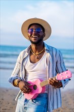 Portrait of black ethnic man enjoy summer vacation on the beach playing ukulele by the sea