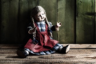 Antique porcelain doll on rustic board floor in front of green wooden wall