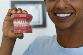 Close-up cropped image of a young man showing a mock-up of teeth with a perfect smile. Concept of whitening