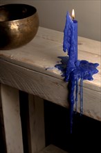 Lighted blue candle melted on a wooden table with a Tibetan bowl in the background