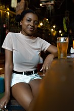 Portrait vertical of young black woman with afro hairstyle looking at camera sitting in a bar