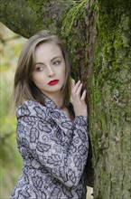 Pensive young woman leaning against a tree looking away