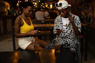 Young afro couple ignoring each other in a bar while using mobile phones