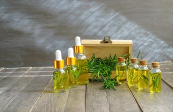 Bottles in a row with droppers of rosemary essential oil with a wooden box and fresh rosemary branches