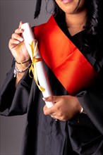 Female student in a graduation photo. End of education degree with graduate diploma. University with black robe holding diploma with hand