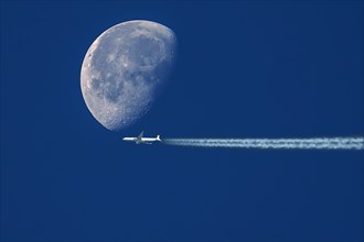 Plane with contrails in front of waning moon in early morning sky