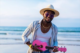 Black ethnic man playing ukulele by the sea enjoying summer vacation on the beach