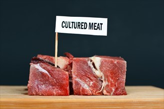 Big raw red meat chunks on wooden plate with label saying 'cultured meat'