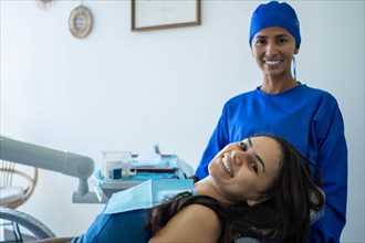 Beautiful young woman smiles sitting in the dentist's chair. She and her doctor look at the camera happy with the result of orthodontic treatment