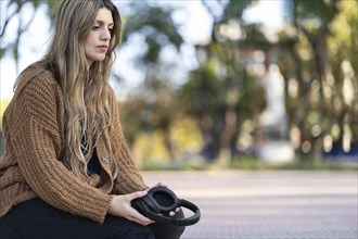 Young woman sitting in a park with a worried expression and a lost look while holding headphones