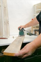Woman's hands sanding a wooden board with an electric sander in her workshop at home