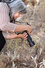 Close-up of a woman photographer with white hair taking a picture of a flower in the field