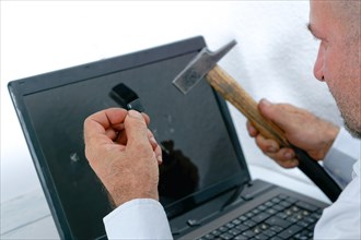 Angry man seen in profile breaking a laptop with a hammer