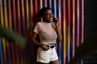Smiling young african american woman talking with cellphone on wall of metal colors background