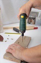 Woman with an electric screwdriver putting screws into a piece of wood