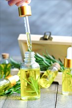 Close-up of a dropper with a drop of rosemary oil in the background several bottles of rosemary essence in a wooden box
