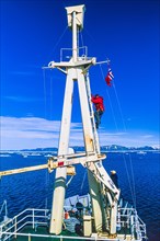 Man climbing up to a lookout on a mast at a ship at arctic sea