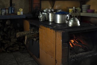 Traditional kitchen with wood stove burning and metal pots. Blurred background