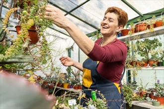 An older woman with short reddish hair smiles and examines her plants