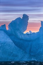 Iceberg in a unique abstract shape in the beautiful colorful sunrise light of the Arctic. Formed over years in a glacier of the Svalbard Archipelago