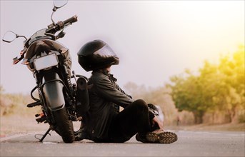 Motorcyclist sitting next to his motorcycle on the road. Motorcyclist sitting and leaning on his motorcycle on the asphalt