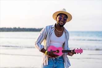 Black ethnic man playing ukulele by the sea enjoying summer vacation