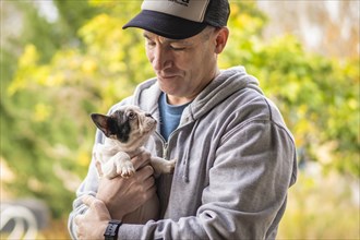 A man hugging a charming french bulldog puppy. Both looking at each other