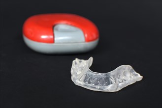 Customized transparent dental teeth bite guard clear aligners for lower jaw in front of blurry case on dark black background