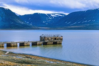 Pier with an old house at an old mine by a fjord village in a mountain coastal landscape Arctic