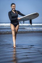 Young woman with prosthesis coming out of the sea with her surfboard. Concept of disability in sport